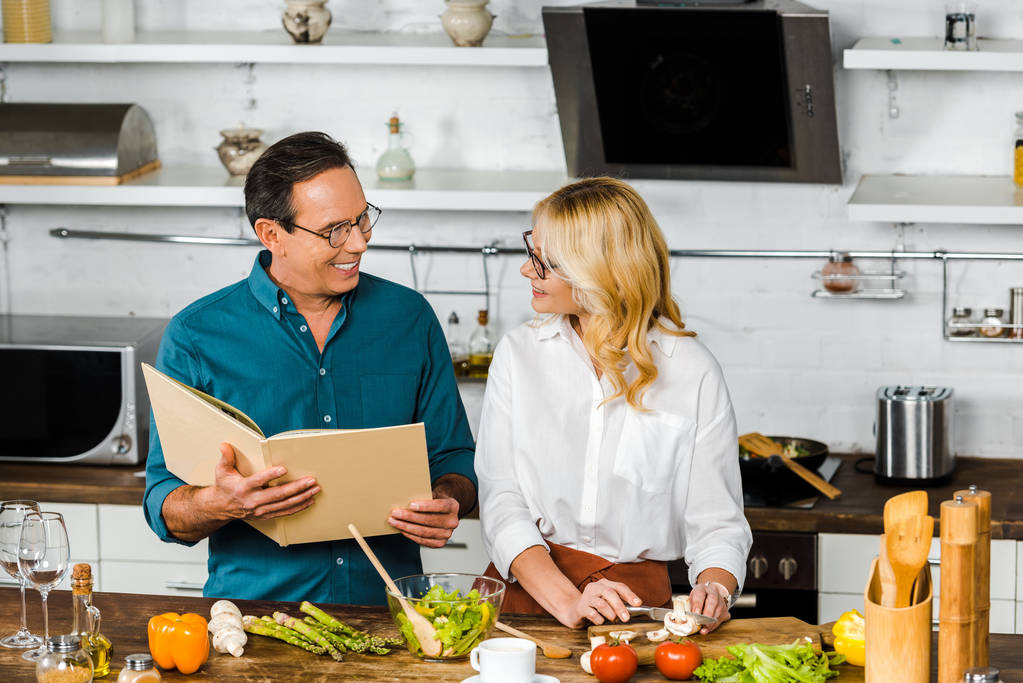 high angle view of mature wife and husband cooking together with cookbook in kitchen - Photo, Image