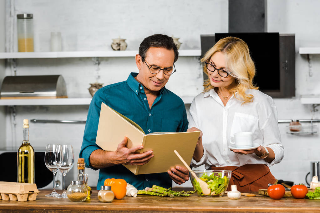 зрелая жена и муж готовят вместе с поваренной книгой на кухне
 - Фото, изображение