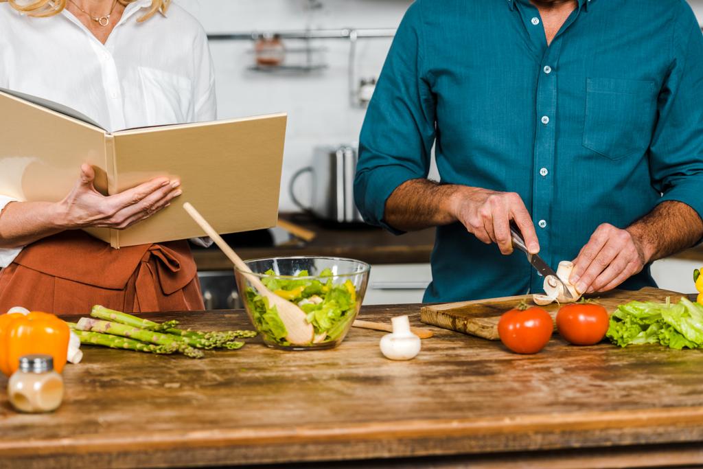 обрезанный образ зрелой жены и мужа приготовления пищи вместе с книгой рецептов на кухне
 - Фото, изображение