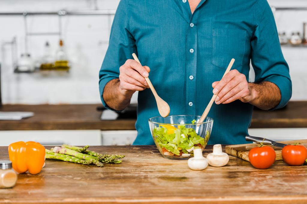 image recadrée de l'homme mûr mélangeant la salade dans un bol dans la cuisine
 - Photo, image