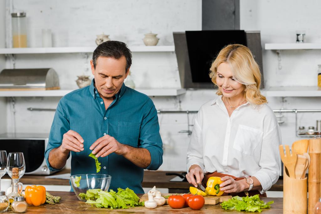 成熟した妻と夫が一緒にキッチンでサラダを調理 - 写真・画像