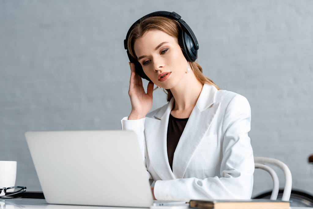 Selektywny fokus piękna bizneswoman w słuchawkach, siedząc przy biurku komputer w miejscu pracy                           - Zdjęcie, obraz