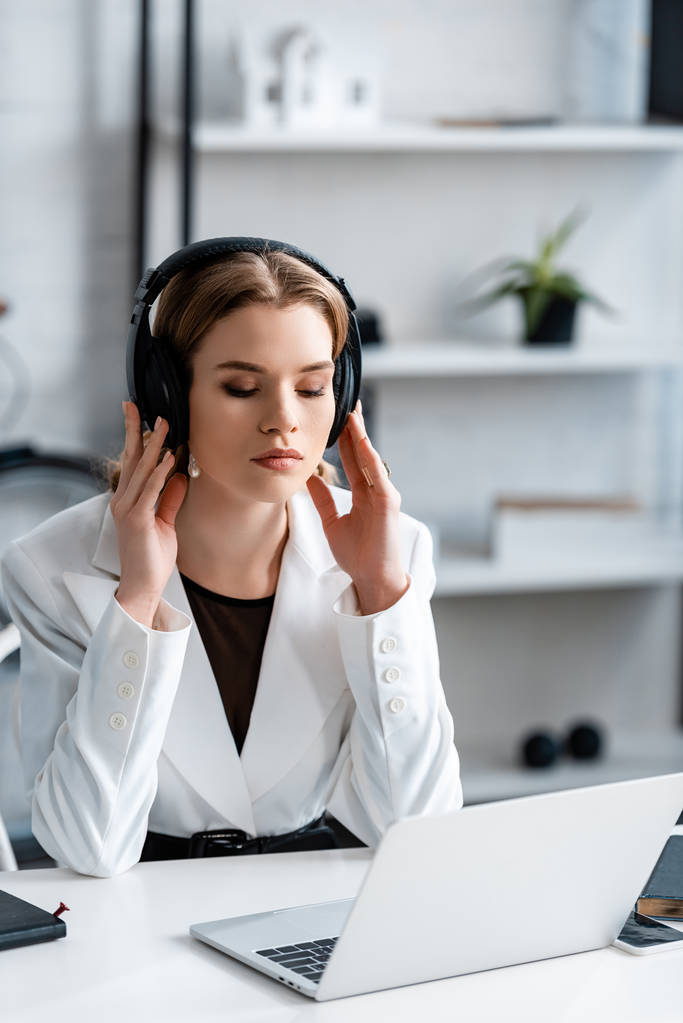 femme d'affaires concentrée dans les écouteurs et vêtements formels assis au bureau de l'ordinateur sur le lieu de travail
                           - Photo, image