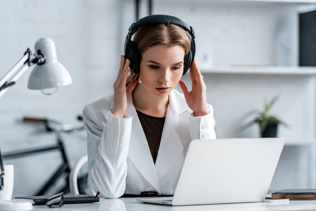 бізнес-леді в навушниках і формальний одяг, сидячи за комп'ютерним столом на робочому місці
                           - Фото, зображення