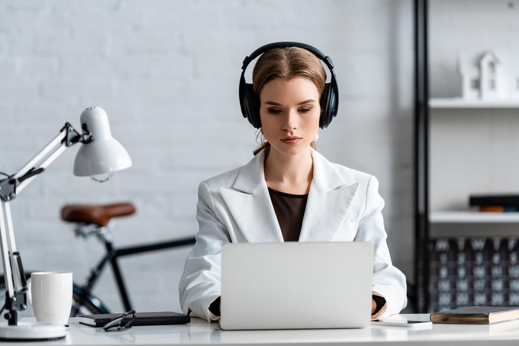 Seriöse Geschäftsfrau mit Kopfhörern sitzt am Computertisch am Arbeitsplatz                           - Foto, Bild
