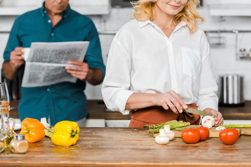 image recadrée de femme mature cuisine et mari lecture journal dans la cuisine
 - Photo, image