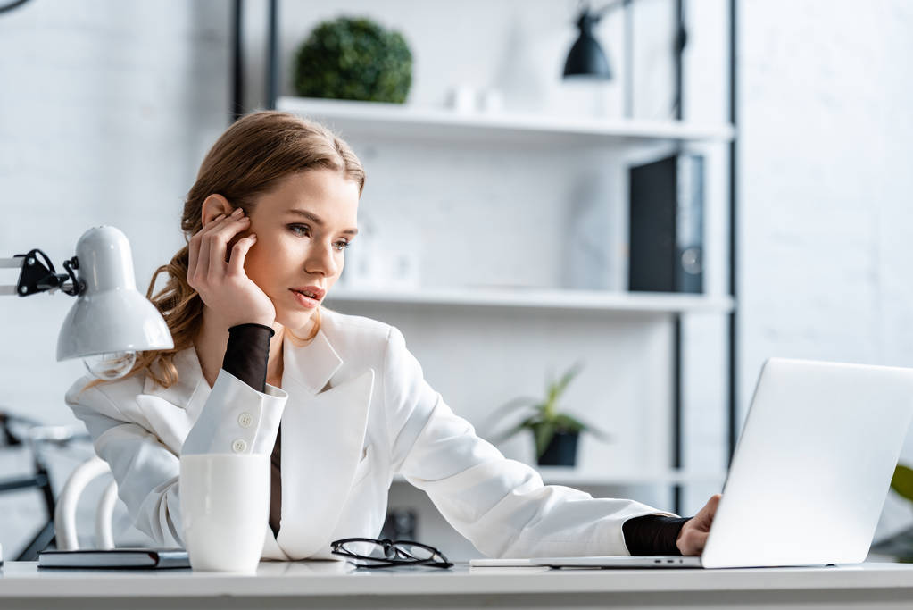 усталая деловая женщина в белой формальной одежде сидит за столом и за компьютером на рабочем месте
 - Фото, изображение