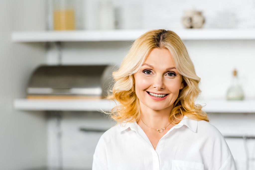 улыбающаяся привлекательная женщина средних лет, смотрящая на камеру на кухне
 - Фото, изображение