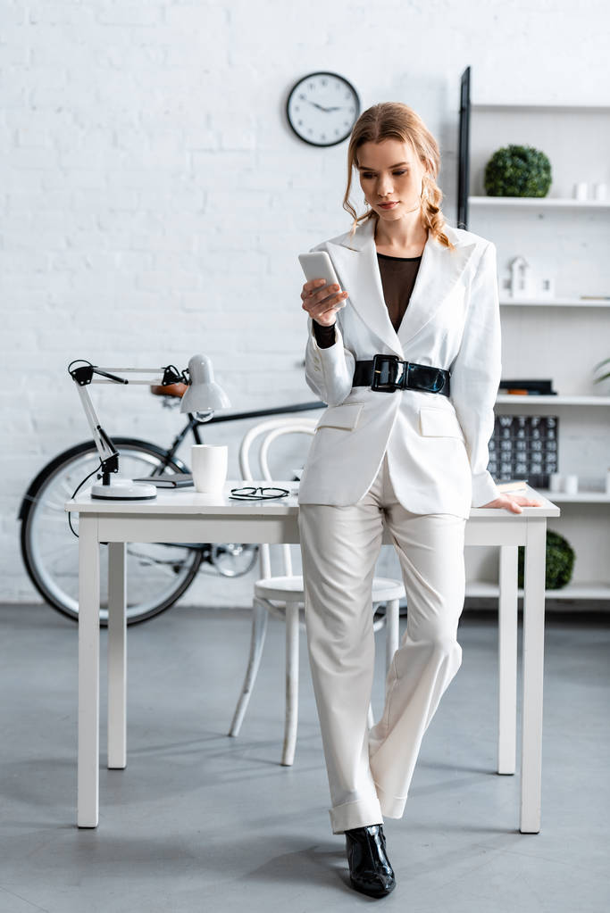 стильная деловая женщина в белой формальной одежде с помощью смартфона на рабочем месте
 - Фото, изображение