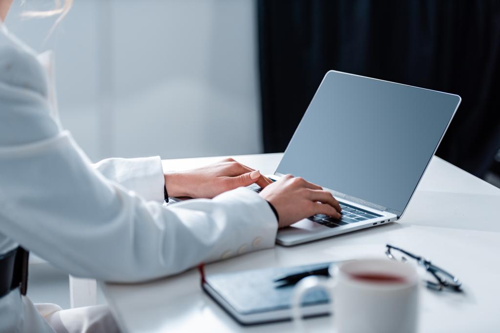 Ausgeschnittene Ansicht einer Frau mit Laptop mit leerem Bildschirm am Schreibtisch im Büro - Foto, Bild