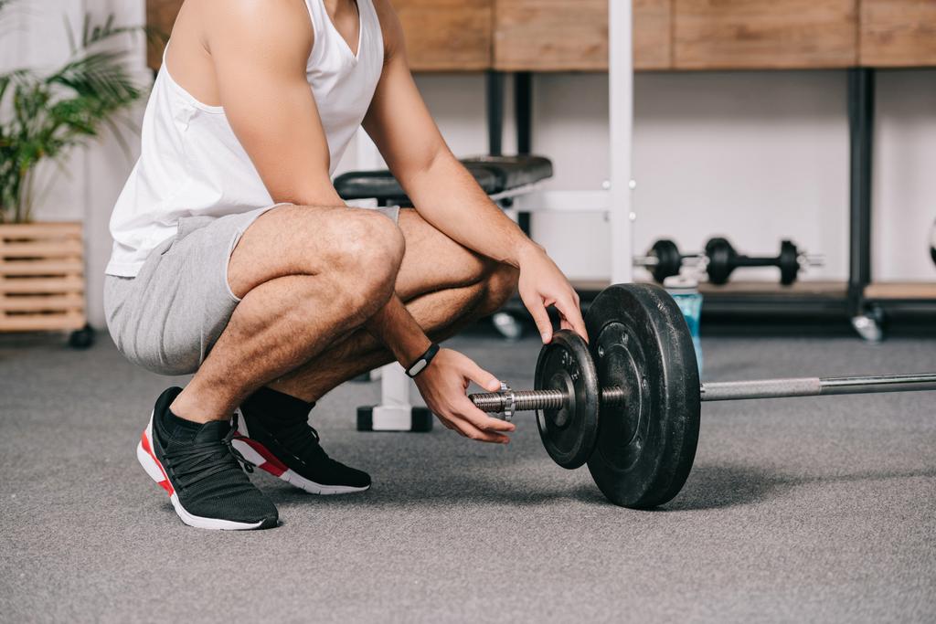 cropped view of man sitting near barbell and putting heavy disk  - Photo, Image
