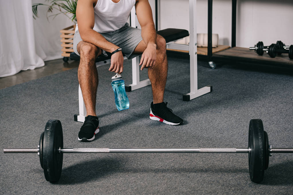 cropped view of man sitting near barbell and holding sport bottle  - Photo, Image