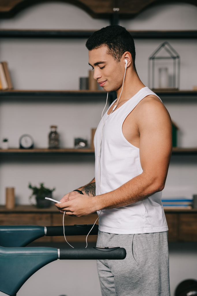 apuesto deportista bi-racial escuchar música en los auriculares mientras se utiliza el teléfono inteligente
  - Foto, Imagen
