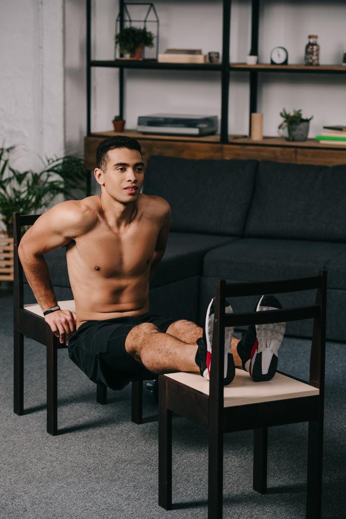 mixed race man exercising on chairs in home gym  - Photo, Image