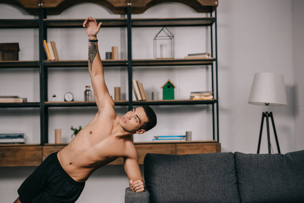 getatoeëerde gemengd ras man doen plank oefening in woonkamer  - Foto, afbeelding