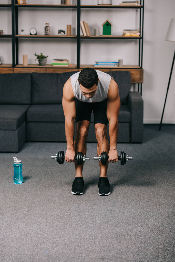 strong mixed race man training with dumbbells in living room  - Photo, Image