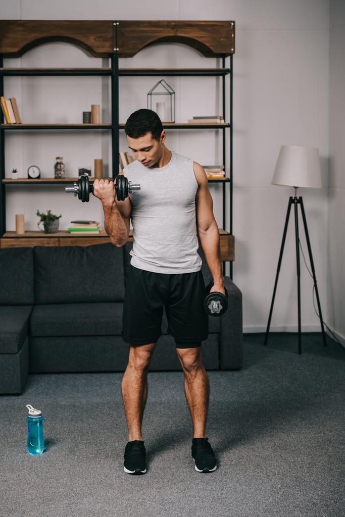 hombre de raza mixta mirando los músculos en la mano mientras hace ejercicio en la sala de estar
 - Foto, Imagen