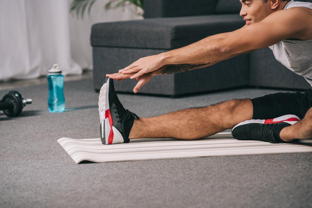 cropped view of mixed race man stretching on fitness mat in living room  - Photo, Image