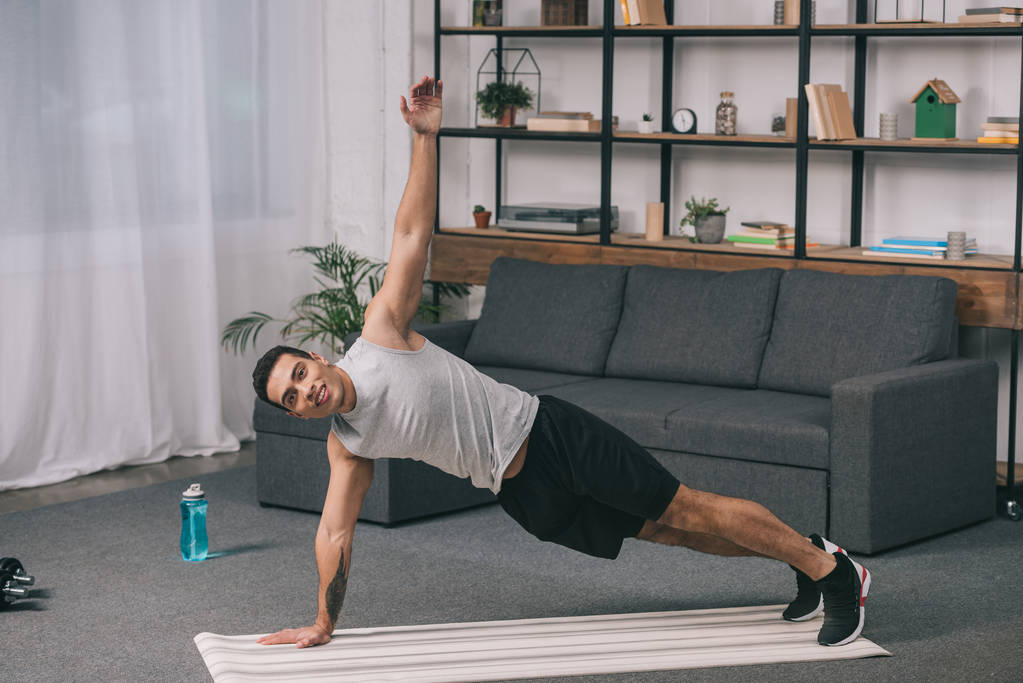 homme bi-racial faisant des exercices de planche sur tapis de fitness dans le salon
  - Photo, image