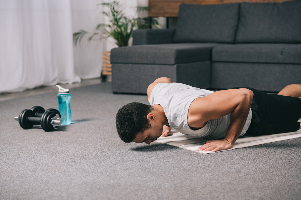 sterke bi-rassen sportman doen oefening op fitness mat in appartement  - Foto, afbeelding