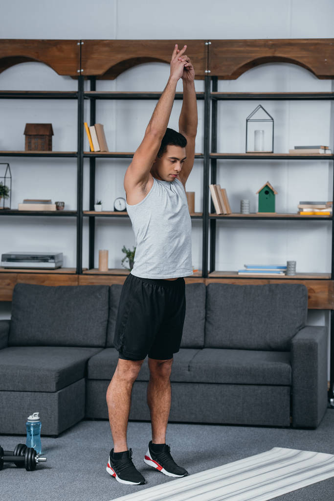 guapo bi-racial hombre de pie cerca de la alfombra de fitness y haciendo ejercicio
 - Foto, imagen