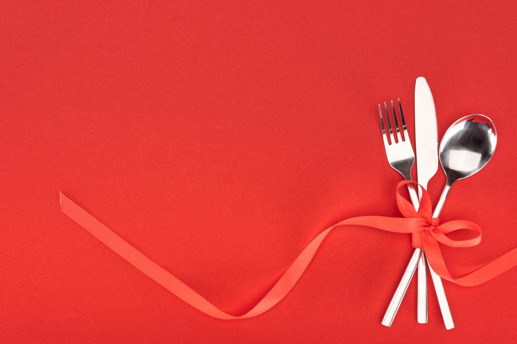 pohled shora na vidličku, nůž a lžíci zabalené červený slavnostní stuha izolovaných na červené, st valentine den koncept - Fotografie, Obrázek