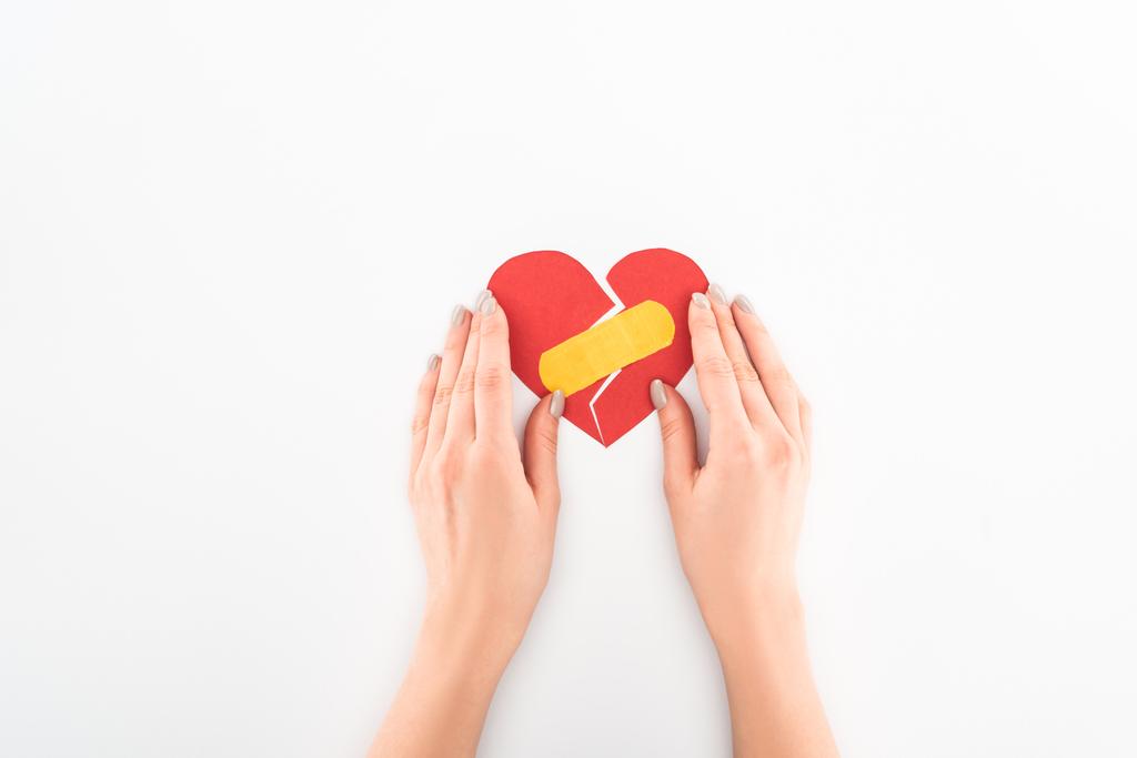 abgeschnittene Aufnahme einer Frau, die ein gebrochenes rotes Herz mit medizinischem Pflaster auf weißem Valentinstag-Konzept trägt - Foto, Bild