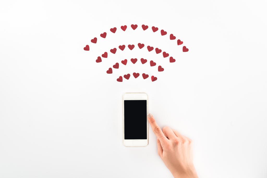 abgeschnittenes Bild einer Frau mit Smartphone mit leerem Bildschirm unter roten Herzsymbolen isoliert auf weißem, Valentinstag-Konzept - Foto, Bild