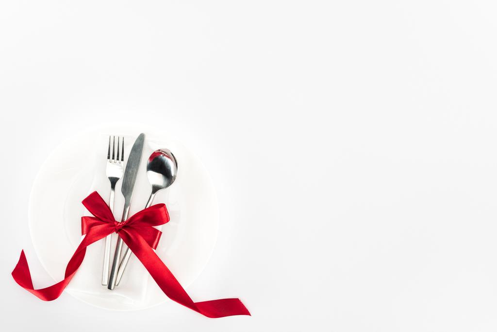 високий вид виделки, ножа і ложки, загорнуті червоним святковим бантом на тарілці ізольовані на білому, концепція дня Святого Валентина
 - Фото, зображення
