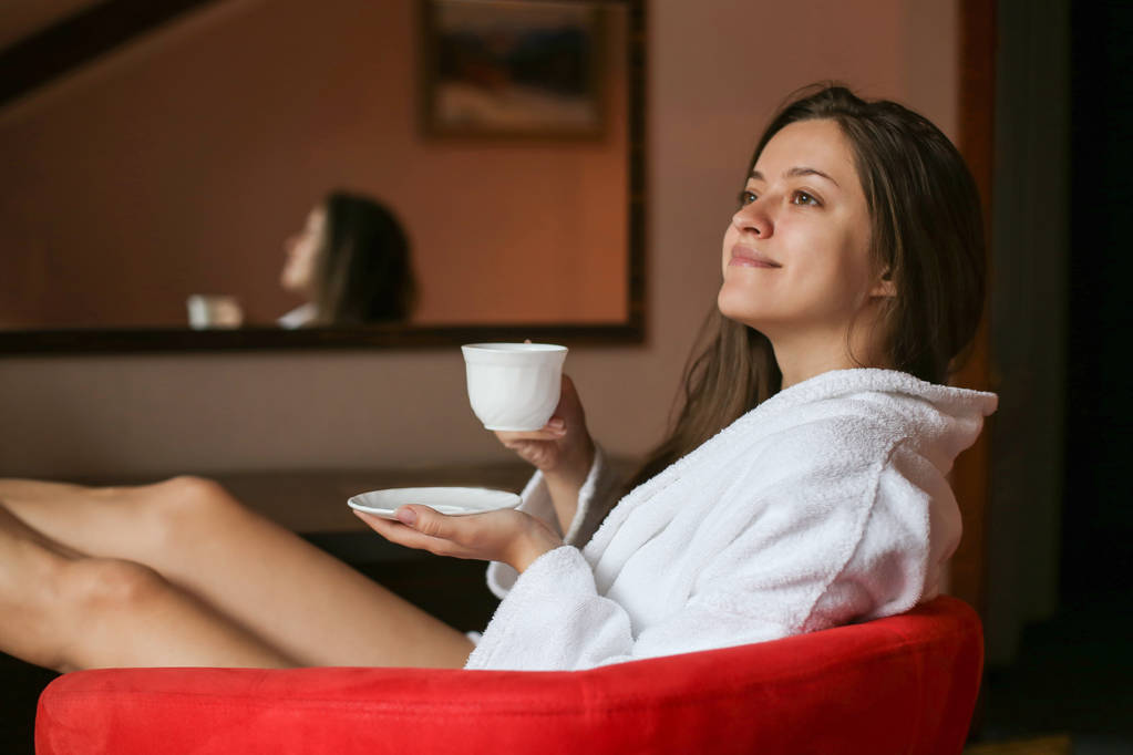 Retrato de la hermosa mujer vestida con un albornoz bebiendo té por la mañana en la habitación del hotel
.  - Foto, imagen