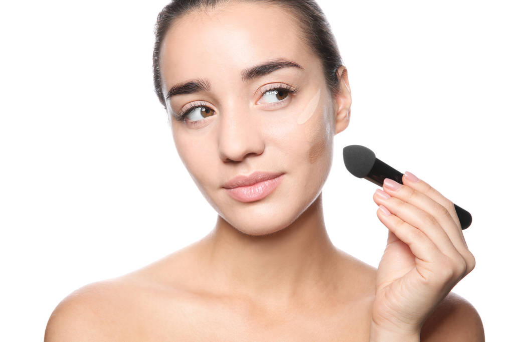 Young woman applying foundation on her face against white background - Photo, Image