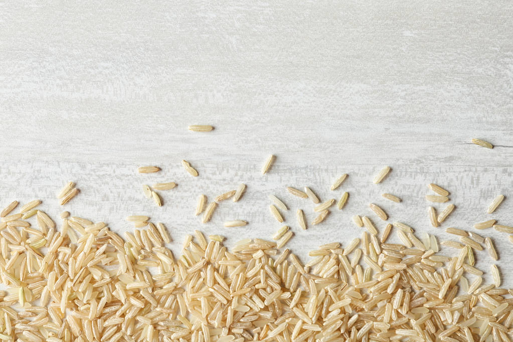 Bruine rijst op houten achtergrond, bovenaanzicht met ruimte voor tekst - Foto, afbeelding
