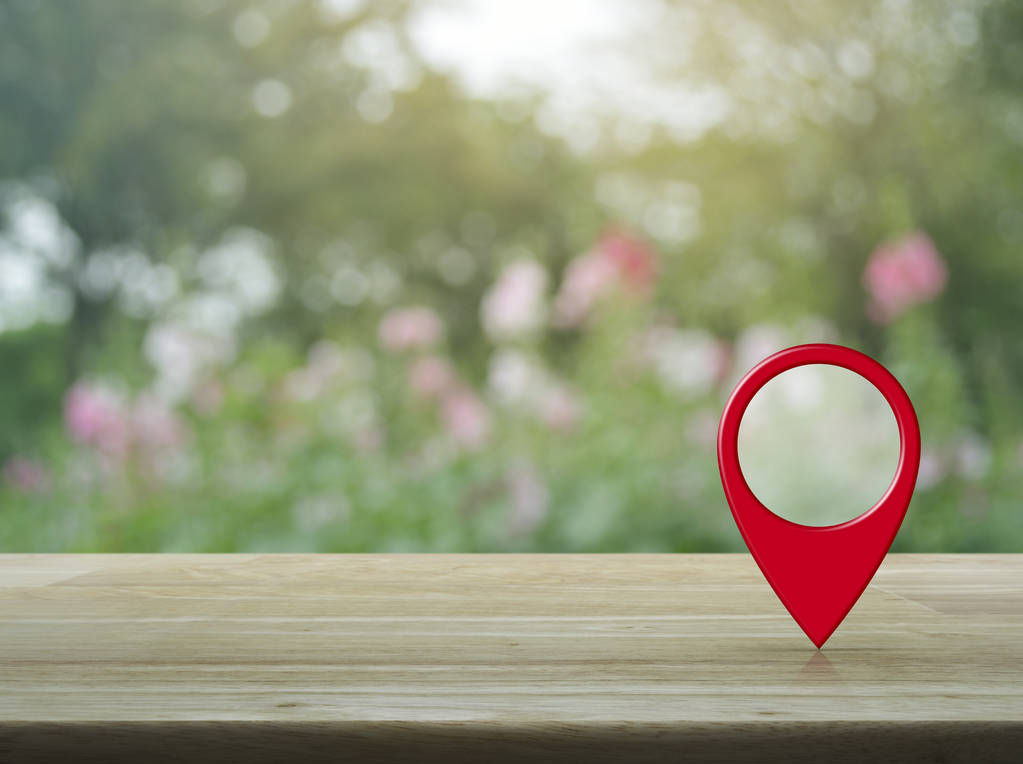 Map pin location button on wooden table over blur pink flower and tree in garden, Map pointer navigation concept - Photo, Image