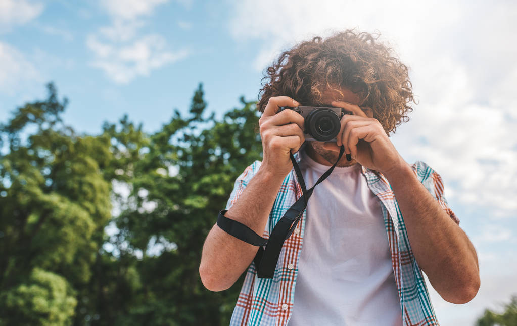Sání Asijské twink muž s digitální fotoaparát fotografování, o povaze a obloha pozadí. Pohledný muž kudrnaté vlasy poznávání přírody na dovolené výlet. Cestování, lidé a životní styl koncepce  - Fotografie, Obrázek