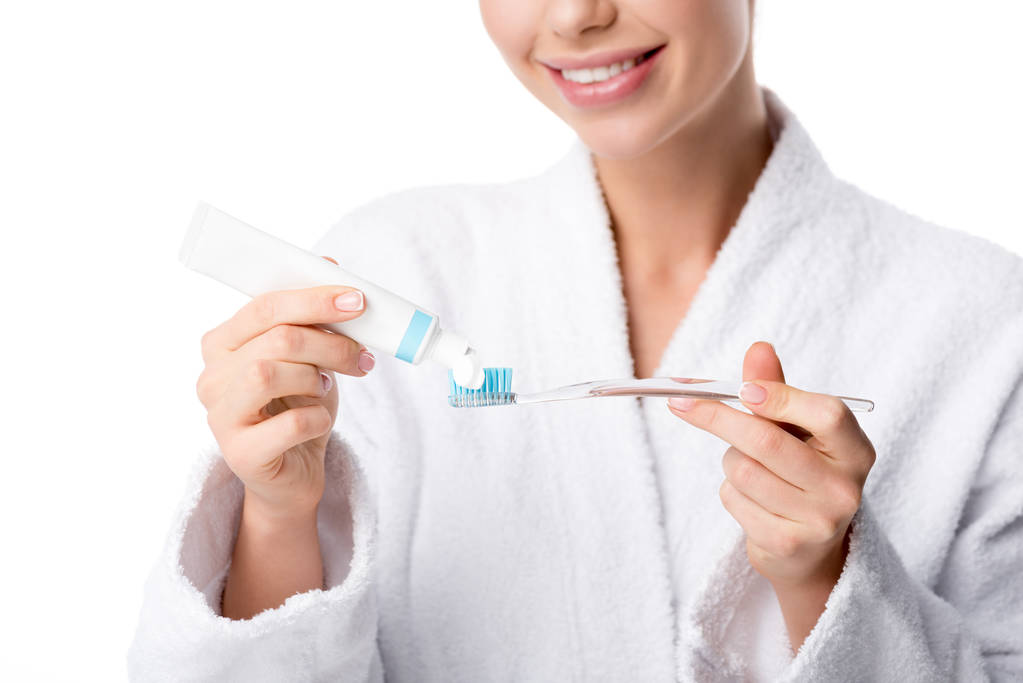 partial view of woman in white bathrobe putting toothpaste on toothbrush isolated on white - Photo, Image