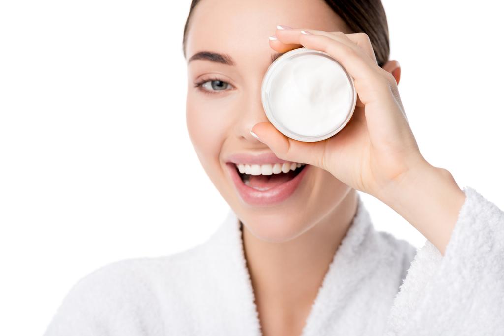 smiling woman in bathrobe holding moisturizing cream in front of face isolated on white - Photo, Image