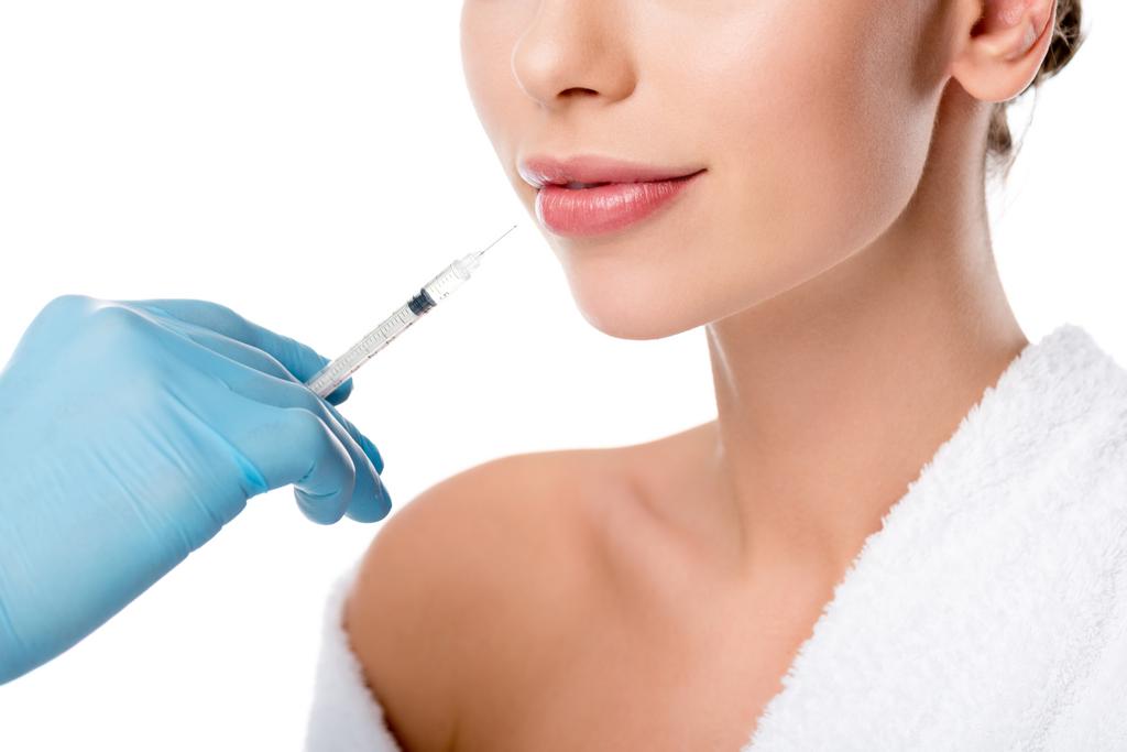 обрезанный взгляд врача в латексной перчатке давая инъекции губ со шприцем женщине изолированы на белом
 - Фото, изображение