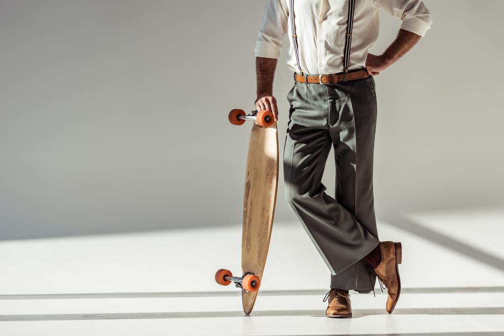 bijgesneden weergave van stijlvolle man houden longboard op grijze achtergrond - Foto, afbeelding
