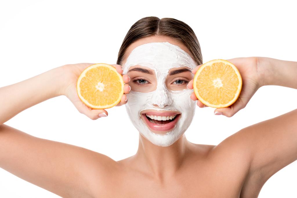 piękna kobieta uśmiechający się z maska Pielęgnacja skóry twarzy przytrzymując pomarańcze i patrząc na kamery na białym tle - Zdjęcie, obraz