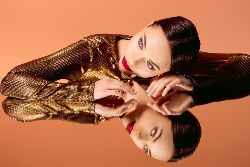attractive woman in golden clothes with glamorous makeup and mirror reflection isolated on orange - Photo, Image