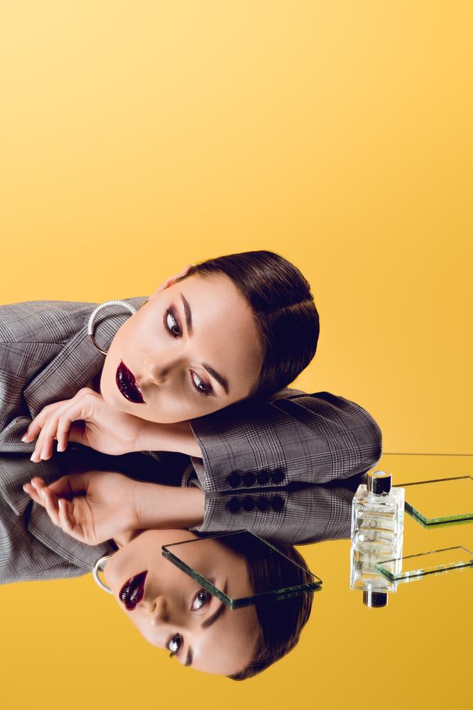 attractive glamorous woman in formal wear with mirror reflection and perfume bottle isolated on yellow - Photo, Image