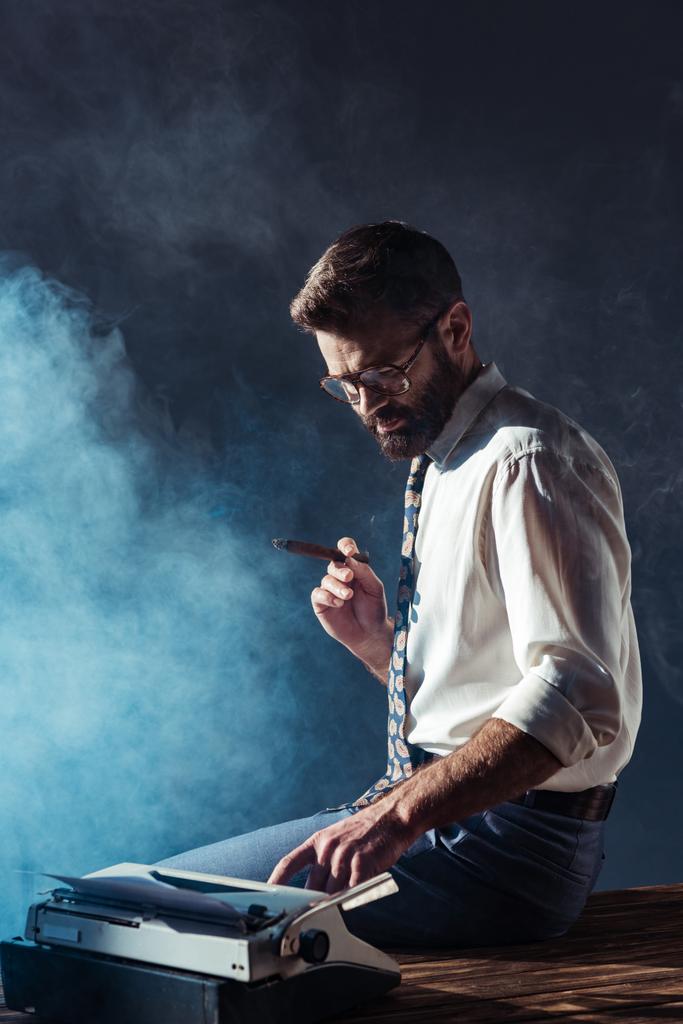κάπνισμα όμορφος άνδρας κάθεται στο τραπέζι με γραφομηχανή - Φωτογραφία, εικόνα