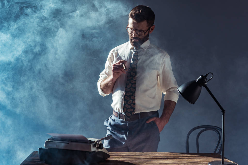 Красивый бородатый мужчина в очках, держит сигару и смотрит на печатную машинку
 - Фото, изображение