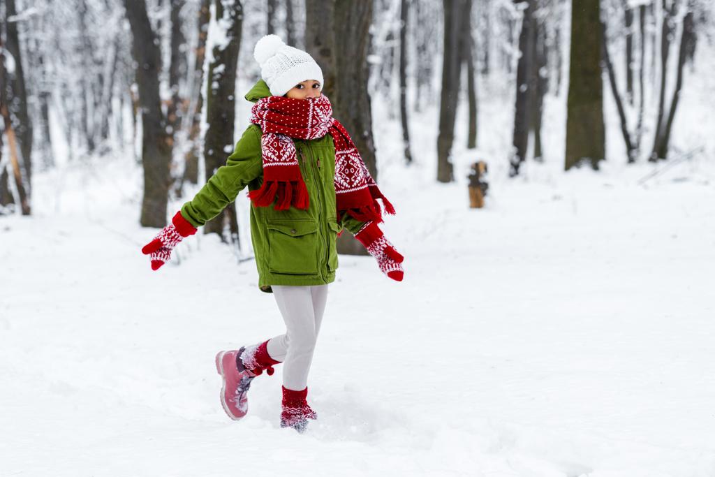Αφρικανική αμερικανική παιδί με ζεστά ρούχα, περπάτημα και να βλέπει την κάμερα στο χειμερινό πάρκο - Φωτογραφία, εικόνα