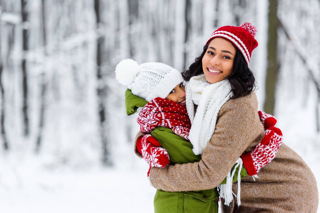 s úsměvem africké americké máma a dcera objímání a při pohledu na fotoaparát v destinaci winter park - Fotografie, Obrázek
