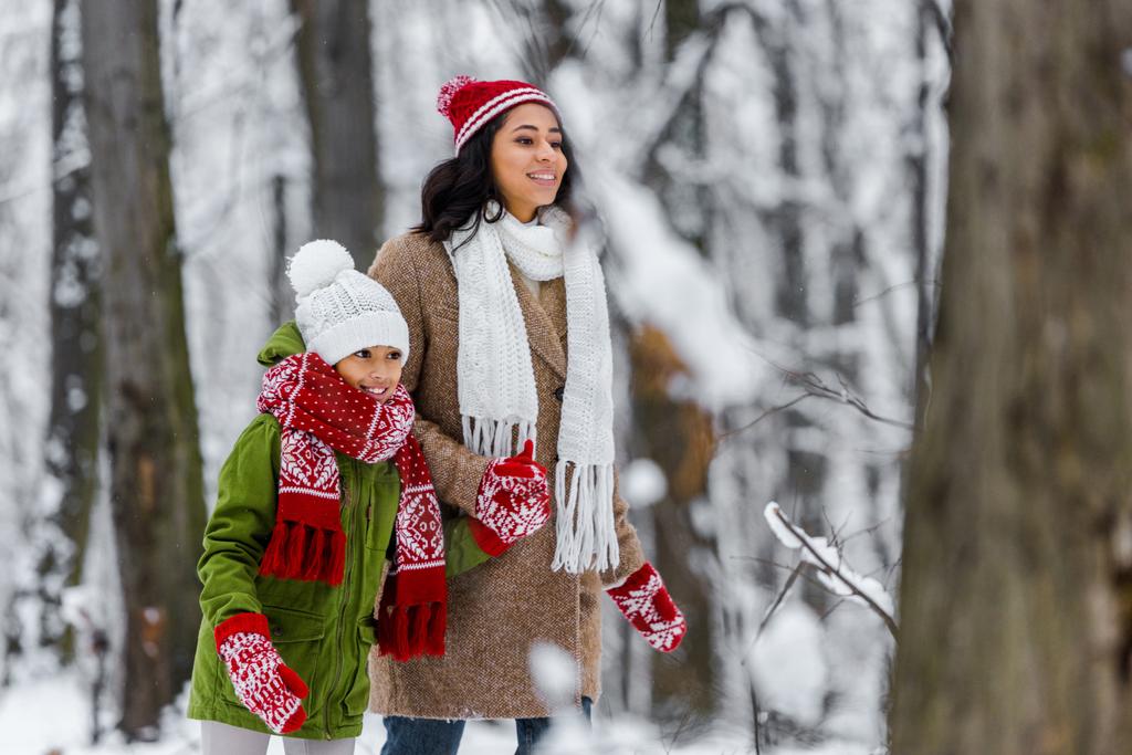 atractiva madre afroamericana y preadolescente hija sonriendo y caminando en el parque de invierno
 - Foto, Imagen