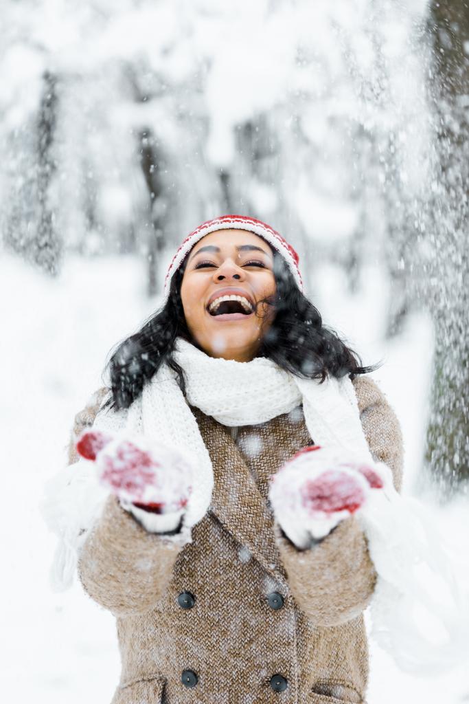 привлекательная американка из Африки бросает снег и улыбается в зимнем лесу
 - Фото, изображение