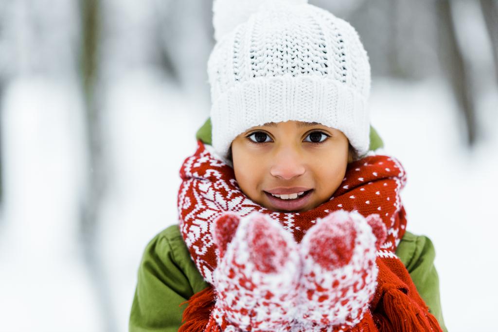 roztomilý africké americké dítě ukazuje bílý sníh na kameru v zimě lese - Fotografie, Obrázek