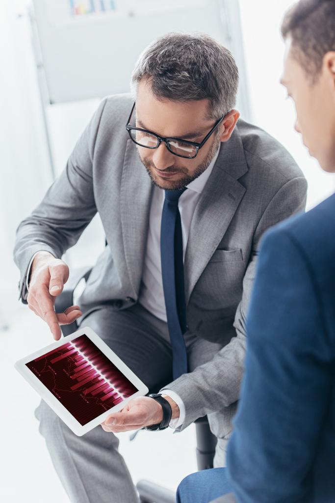 обрезанный снимок бизнесмена в очках, показывающий цифровой планшет с торговыми графиками коллеге-мужчине в офисе
 - Фото, изображение