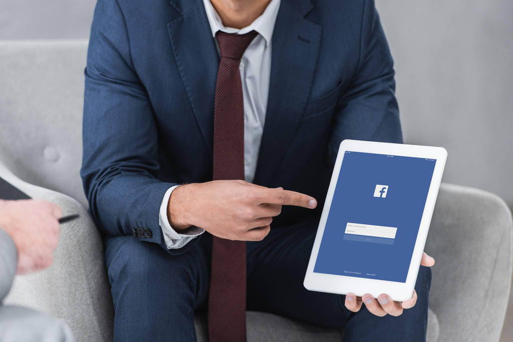 abgeschnittene Aufnahme eines Geschäftsmannes in offizieller Kleidung, der mit dem Finger auf digitales Tablet mit Facebook-App zeigt - Foto, Bild